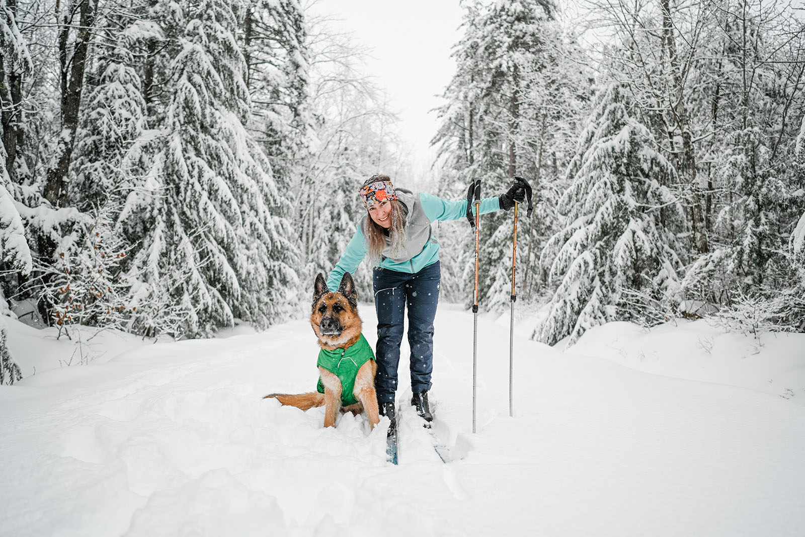 Cross country skier crouches to pet her dog companion