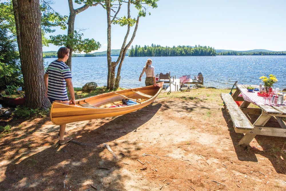 a man and woman carrying a canoe to a lake