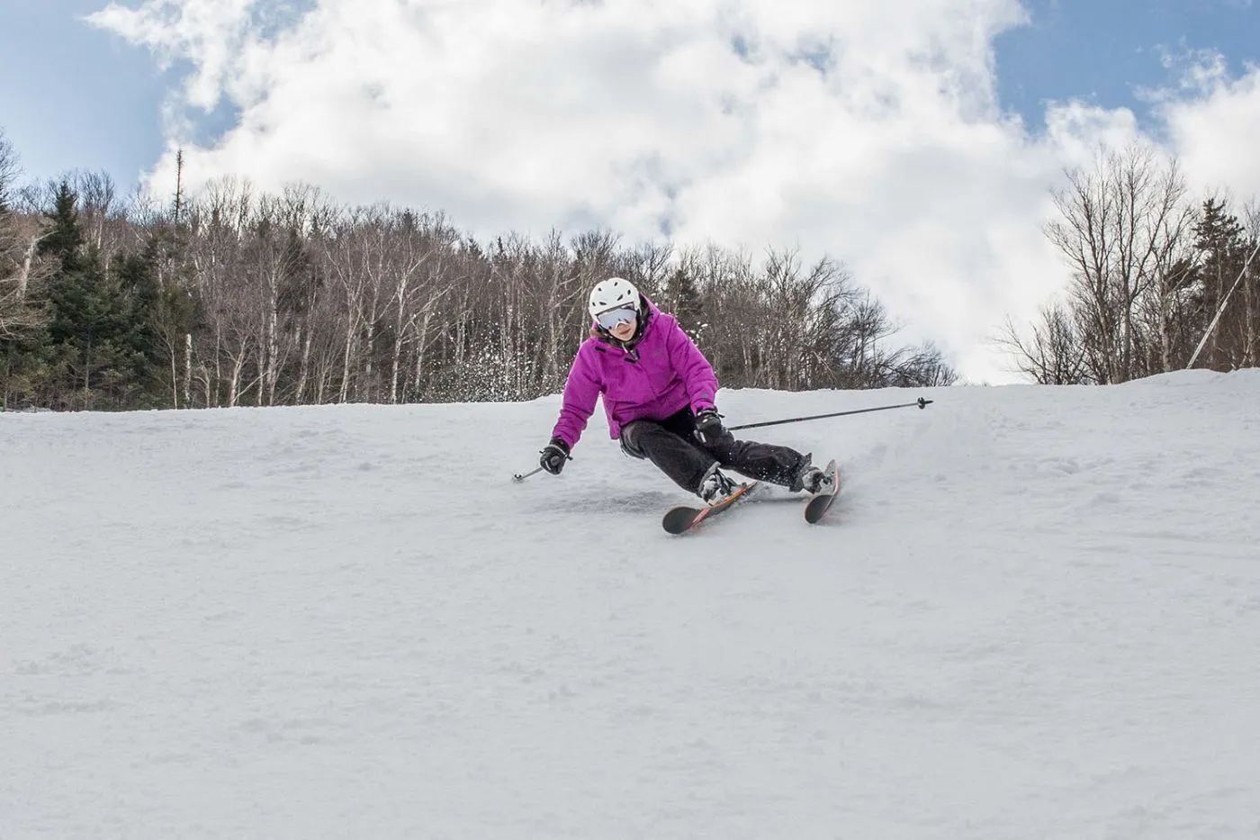 A skier in a pink jacket and white helmet navigates a snowy slope using a sit-ski, leaning into a turn with outriggers for balance