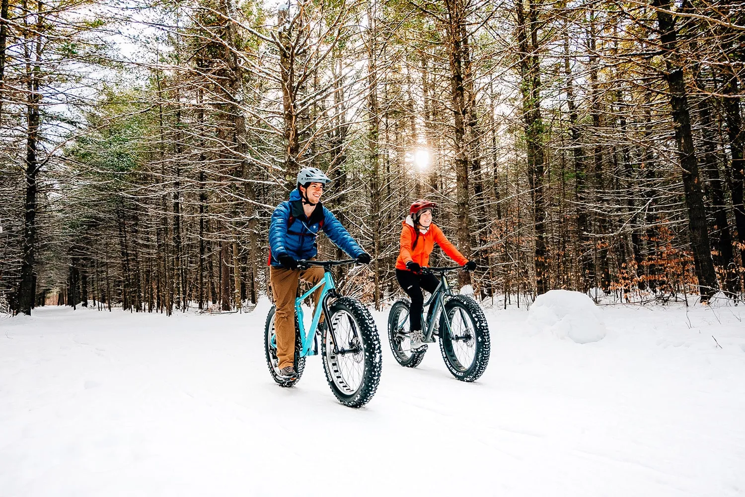 Two people snow biking on a trail through the woods