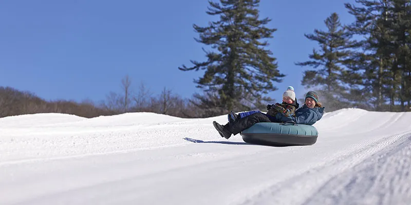 Action shot of a mom and a kid sitting in a tube zooming down a snow-covered hill