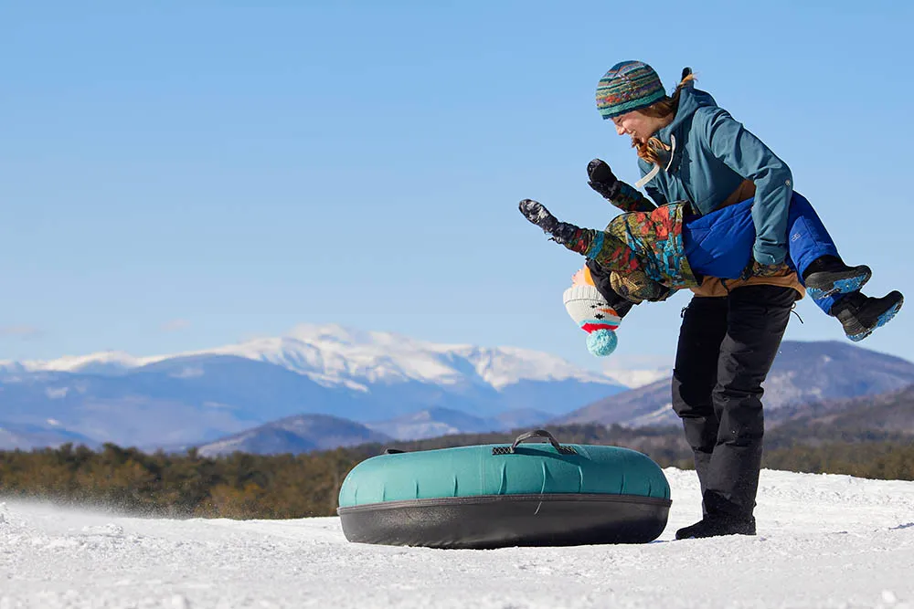 Mom holding her son tipping him back playfully, a snow tube lies ready on the ground